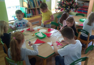 Dzieci przy stolikach przyklejają czerwony trójkąt - czapkę Mikołaja do talerzyka.